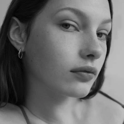 Close-up portrait of a young woman with hoop earrings and dark hair against a plain background