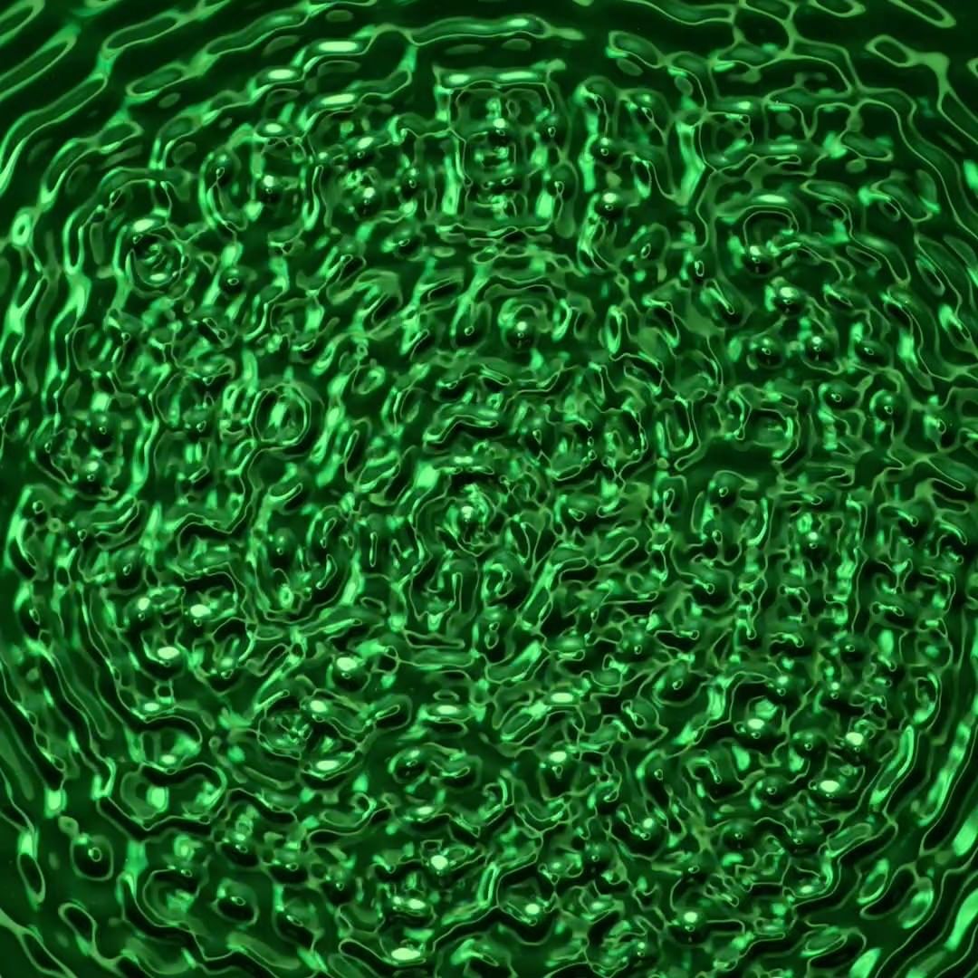 Abstract rippled liquid effect with circular waves in various shades of green and black reflecting light across the surface.