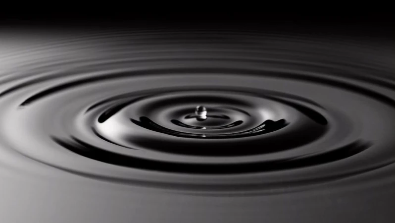 Water drop creates concentric ripples on the liquid surface in a dark setting, reflecting the impact and circular wave patterns.