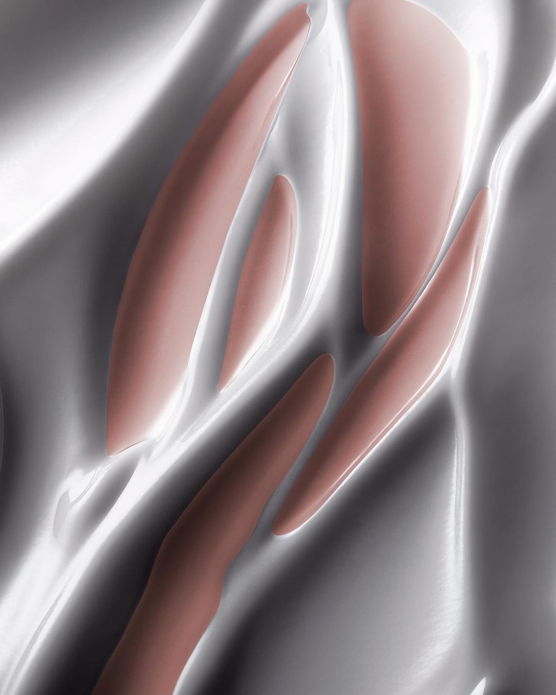 Abstract close-up of flowing, shiny, rose-toned makeup on a metallic, light-reflective surface with soft highlights and shadows.