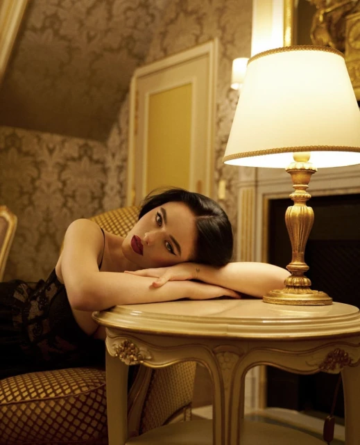 Adult woman with dark hair lies on a table in an ornate room. A lamp sits on the table near her head. Interior design.