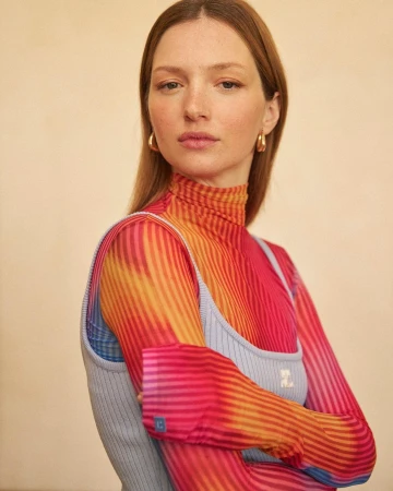 Portrait of a woman wearing a colourful striped sheer turtleneck top under a light blue ribbed tank top by Pauline Darley
