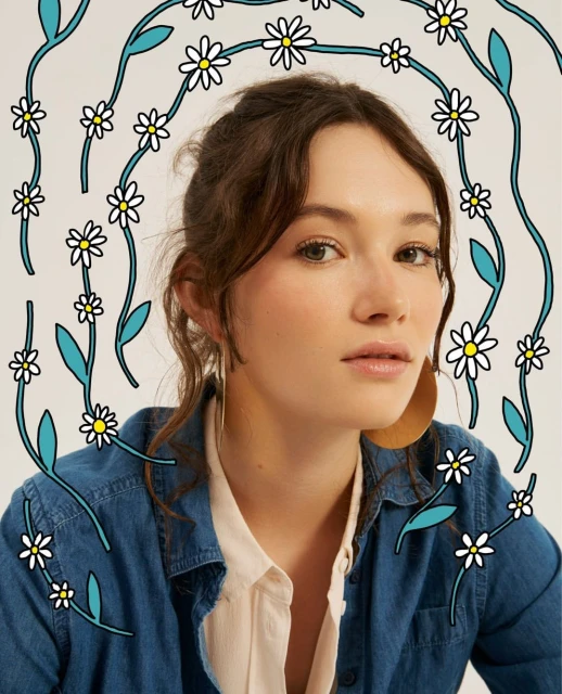 Portrait of a young woman wearing a denim shirt and large hoop earrings, adorned with illustrated daisy flowers and leaves.