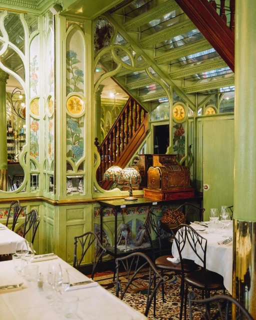 Art Nouveau style restaurant interior with ornate woodwork, mirrored walls, dining tables set with white linens and glassware.