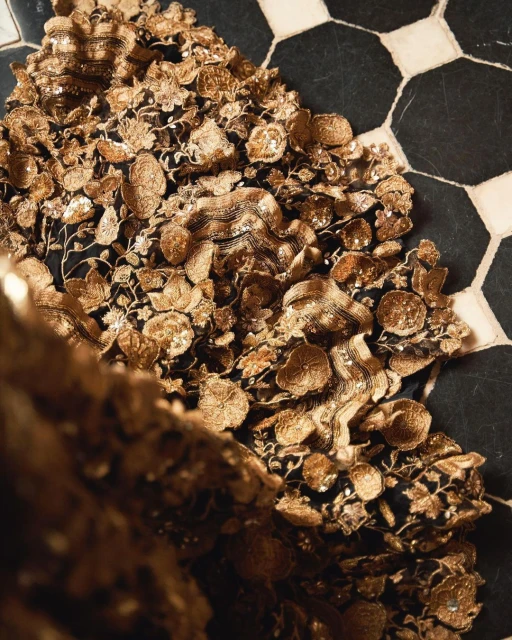Close-up of an ornately designed gold gown featuring floral and wave patterns placed on an octagonal black and white tile floor.