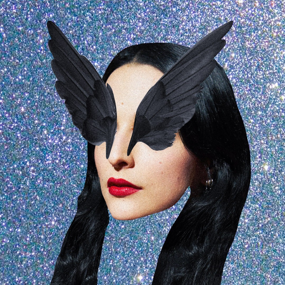 Artistic studio shot of a woman with black hair and red lipstick wearing feathered wings over her eyes against a sparkly blue background.