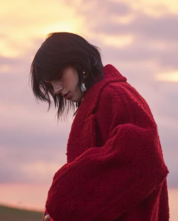 Woman in a textured red coat posing outdoors against a sunset sky by photographer Pauline Darley