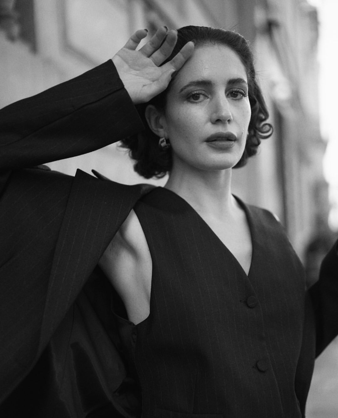 Black and white portrait of a woman in a black blazer. The woman is posing with her hand above her head.