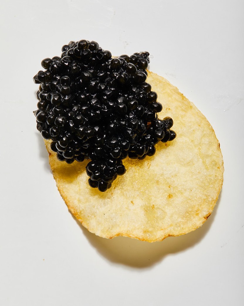 Close-up shot of black caviar atop a golden potato chip against a white background, highlighting the delicacy's texture and color contrast.