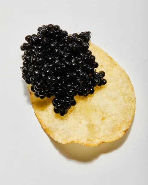 Close-up shot of black caviar atop a golden potato chip against a white background, highlighting the delicacy's texture and color contrast.