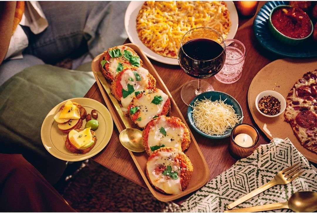Overhead shot of a rustic wooden table featuring assorted pizzas, appetizers, red wine, and a lit candle, creating a cozy atmosphere.