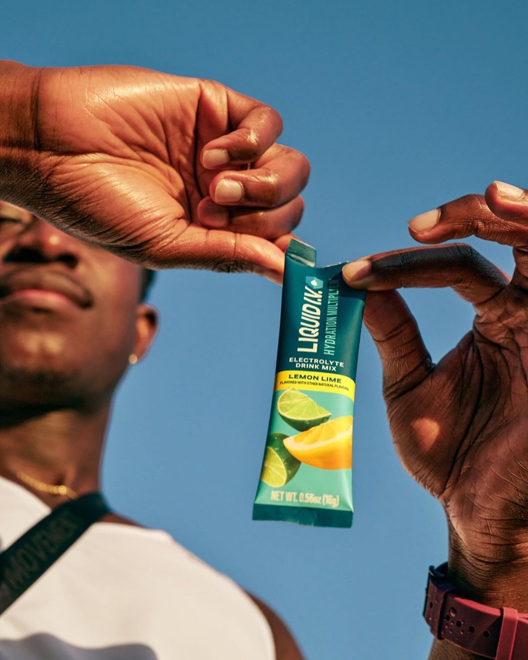 Close up of an athletic African-American male holding a Liquid I.V. Electrolyte drink mix in front of a bright blue sky background.