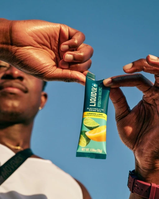 Close up of an athletic African-American male holding a Liquid I.V. Electrolyte drink mix in front of a bright blue sky background.