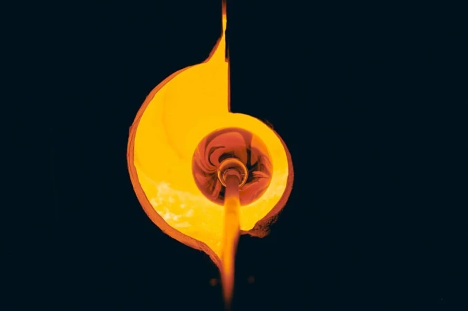 Abstract studio shot of molten glass art, featuring flowing, organic forms glowing with orange and yellow hues against a dark background.