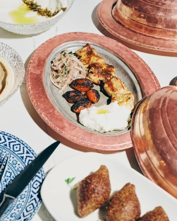 Overhead shot of a copper serving plate with grilled meat skewers, onions, tomatoes, and puree, accompanied by other Middle Eastern dishes.