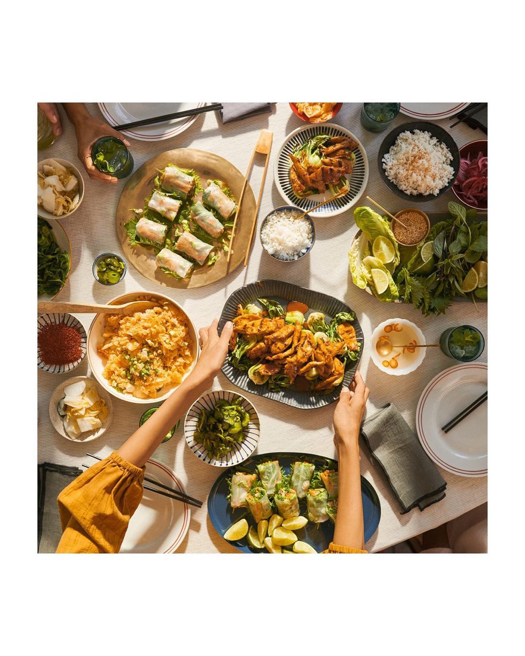 Overhead shot of a table filled with plates of various Asian-inspired dishes, including rice paper rolls, kimchi, and seasoned meat.