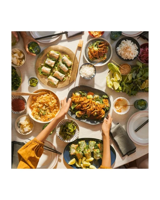 Overhead shot of a table filled with plates of various Asian-inspired dishes, including rice paper rolls, kimchi, and seasoned meat.