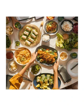 Overhead shot of a table filled with plates of various Asian-inspired dishes, including rice paper rolls, kimchi, and seasoned meat.