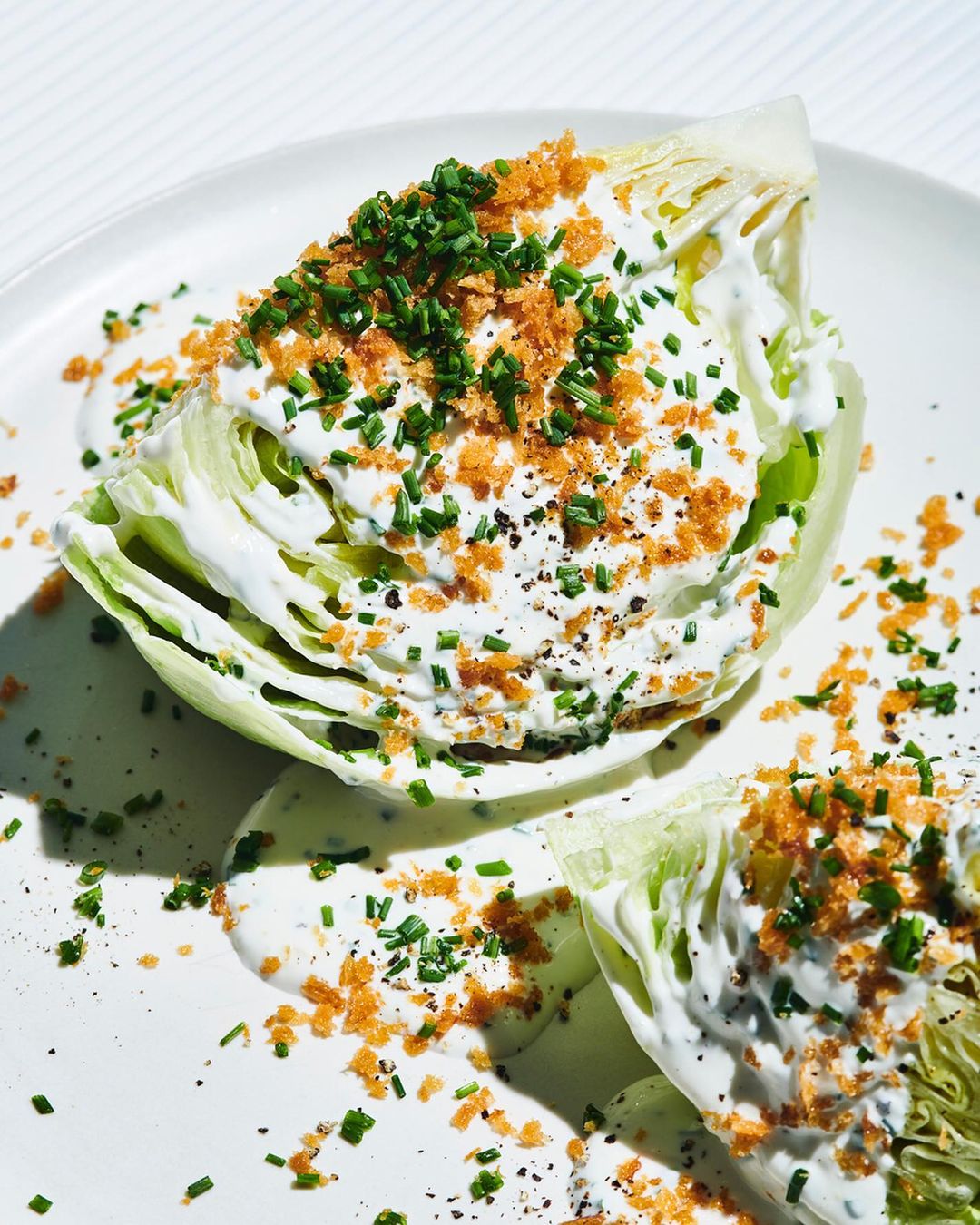 Overhead view of a wedge salad with creamy dressing, chives, and breadcrumbs on a white plate. Food photography highlighting fresh ingredients.