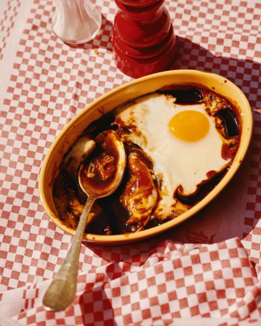 Overhead shot of a cooked egg on top of a dish with brown gravy, served on a red and white checkered tablecloth.