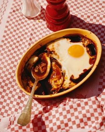 Overhead shot of a cooked egg on top of a dish with brown gravy, served on a red and white checkered tablecloth.