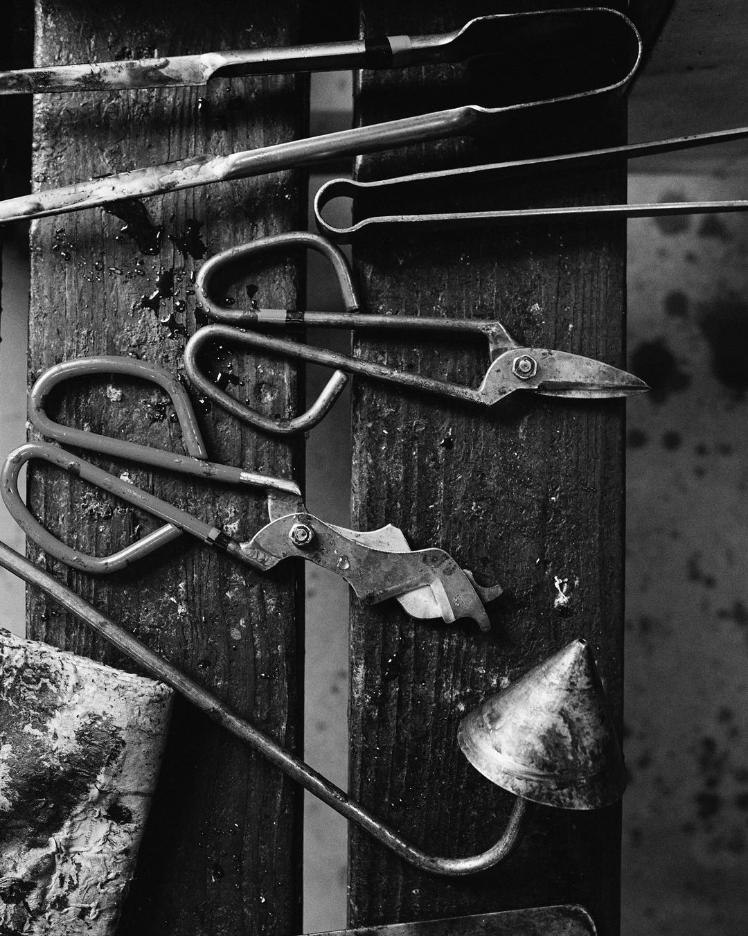 Vintage metal tools including metal shears, pliers, and a funnel with wooden planks in a vertically-oriented, monochrome composition.