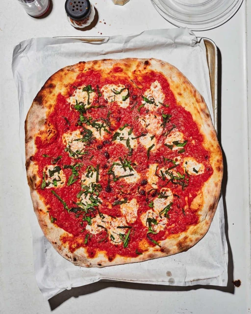 Overhead shot of a freshly baked pizza with tomato sauce, mozzarella, and basil leaves on parchment paper, ready to be served.