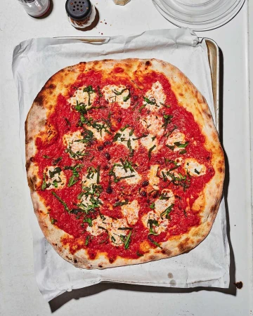 Overhead shot of a freshly baked pizza with tomato sauce, mozzarella, and basil leaves on parchment paper, ready to be served.