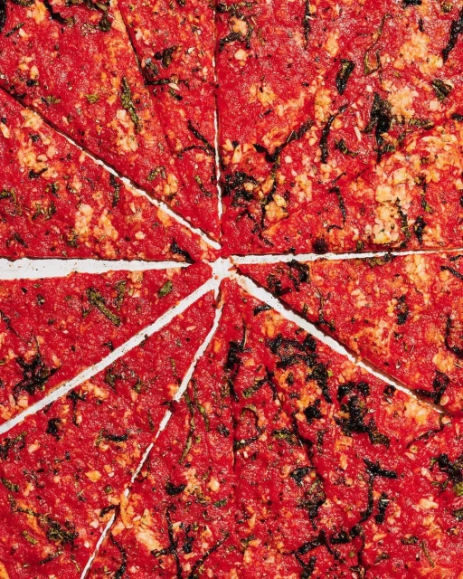 Overhead view of a food flat lay featuring a tomato-based sauce dish cut into triangular pieces, showcasing a rich, vibrant texture.