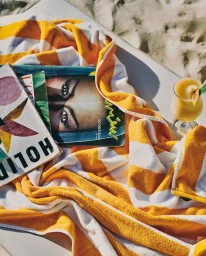 Yellow and white striped beach towel with two magazines and a yellow cocktail glass on sand