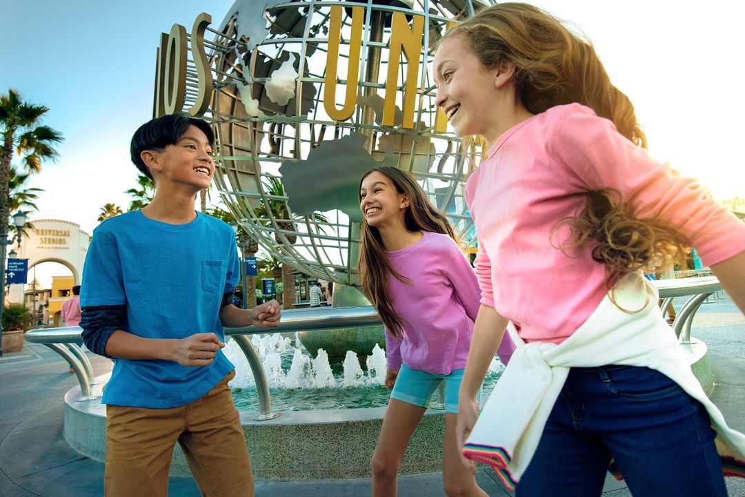 Three smiling teenagers stand in front of Universal Studios globe and fountain on a sunny day, showcasing positive interactions and leisure.