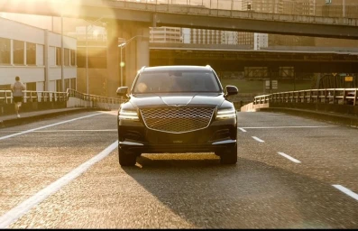 A black luxury SUV parked in the center of an empty multilane road with an overpass bridge and warm golden hour sunlight.