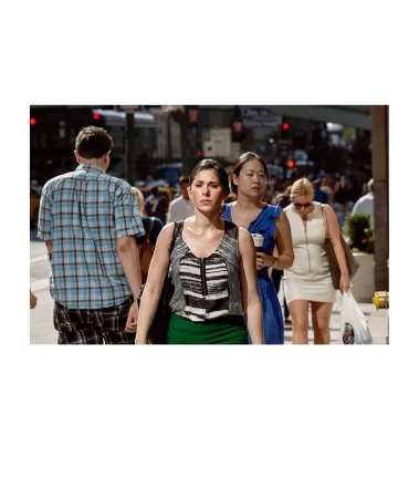 Urban street scene featuring a woman in a striped top and green skirt, with diverse pedestrians in the background on a sunny day.