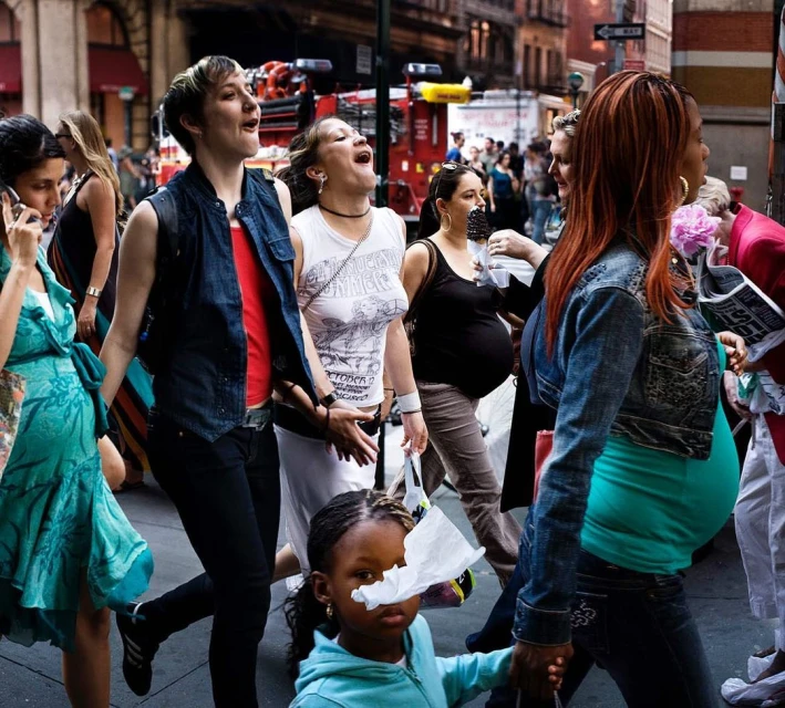 Candid street-style scene in New York City showcases a diverse group of pedestrians walking. Focus on a child with a tissue on her face.