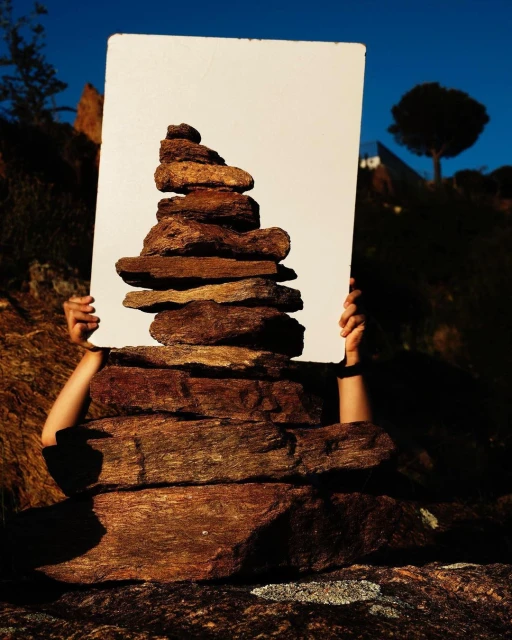 Stacked rock cairn held by hands against a blue sky. Artful and creative zen-like composition with a nature background and brown rocks.