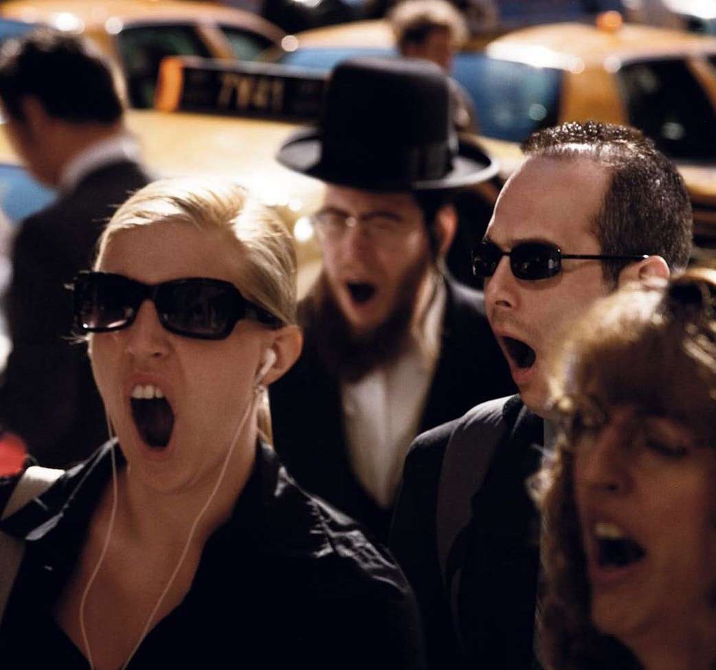 Street scene captures a group of people yawning in unison, with blurred taxis in the background, creating a candid and relatable moment.