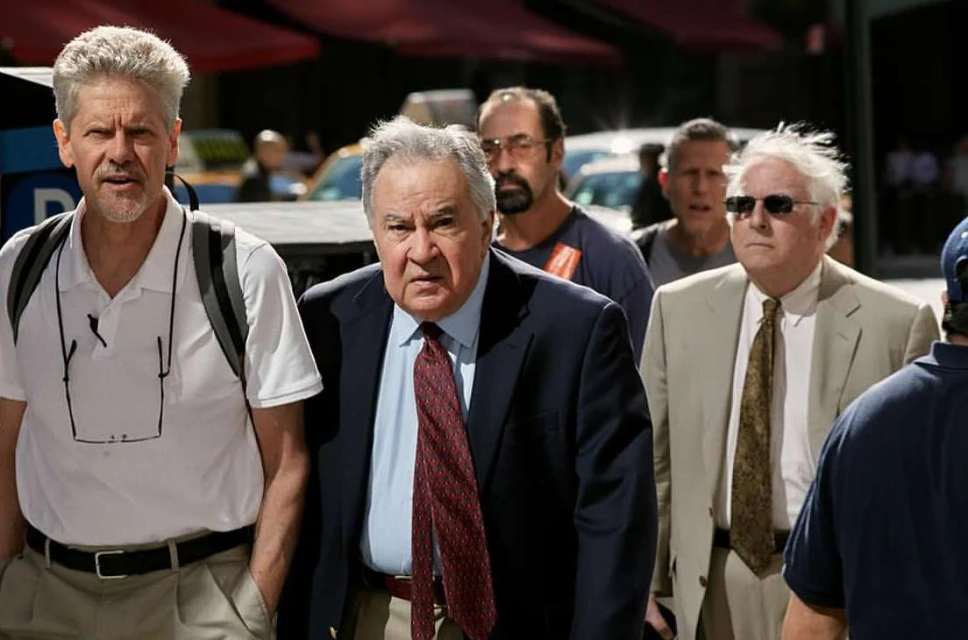 Group of men walking outdoors in an urban setting, wearing suits, and casual attire, with city street and buildings in the background.