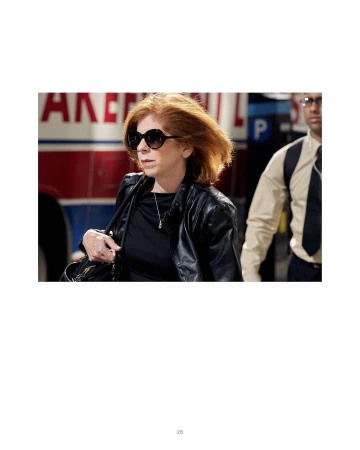 Red-haired woman in sunglasses and a black leather jacket walking past a bus, photographed by Peter Funch in Berlin.