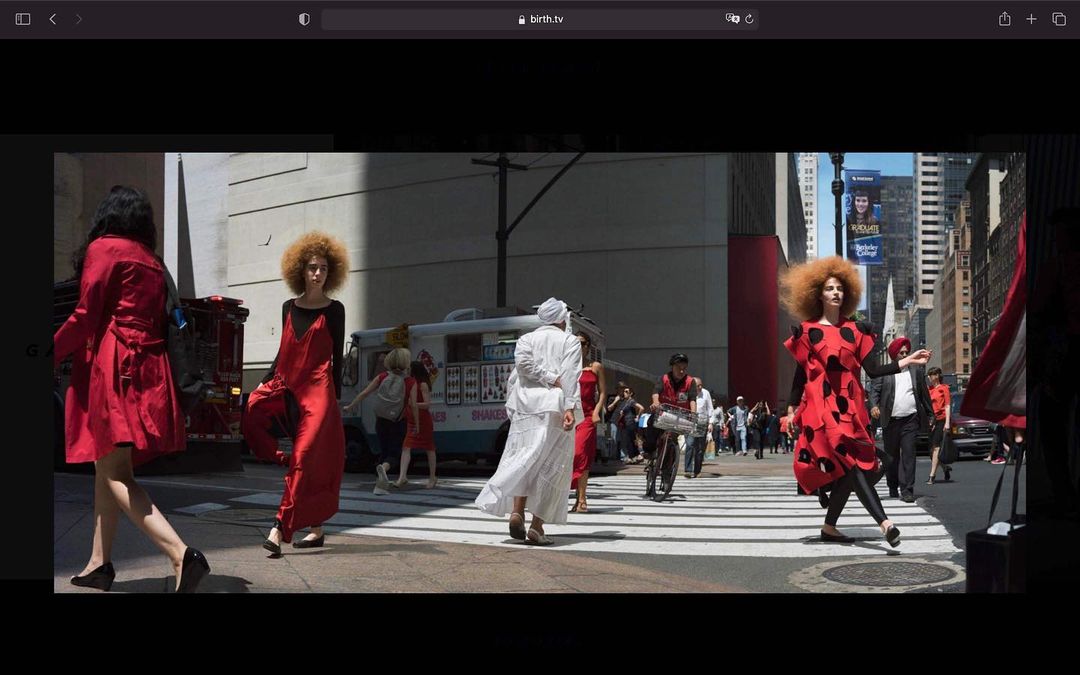 Fashion editorial photo of diverse women in red and white dresses walking on a city street crosswalk with city buildings and a food truck.