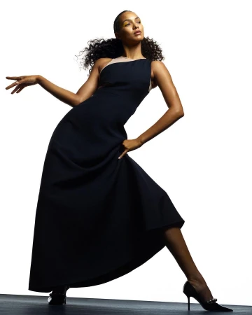 Model wearing a dark sleeveless long dress and pointed-toe heels posing in a dynamic stance against a white background