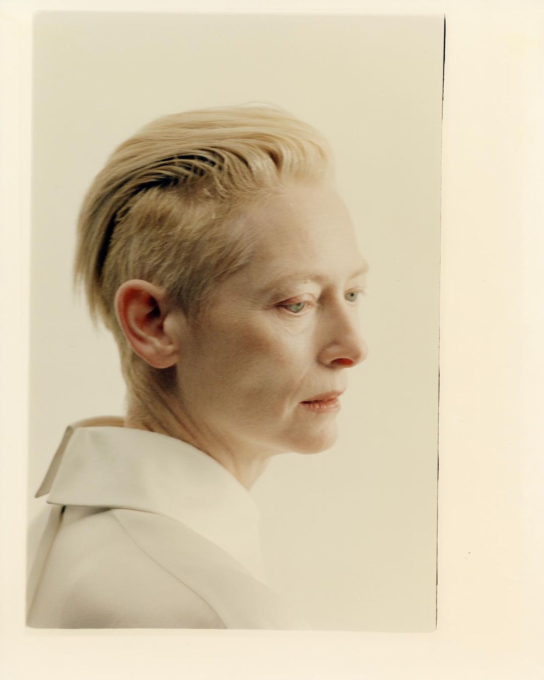 Headshot of an adult female with an undercut hairstyle and neutral facial expression wearing a white collared shirt in a studio.