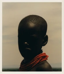 Portrait silhouette of a child wearing a layered red bead necklace against an overcast sky, captured by Peter Jordanov