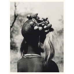 Monochrome portrait from behind of a person with botanical head adornments, beaded necklaces, and large earlobe stretching.