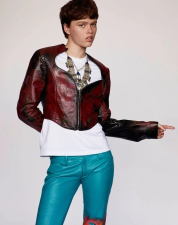 Model in dark red cropped jacket, white t-shirt, and blue pants against white background