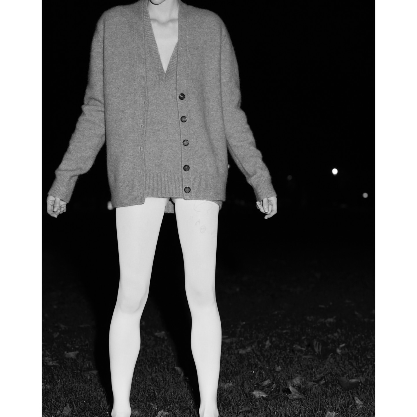 Model wearing a grey cardigan and v-neck sweater with white tights standing outdoors at night by Peter Joseph Smith