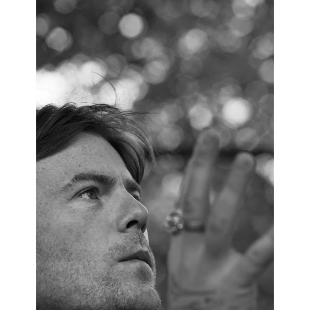 Monochrome portrait of an adult male in profile, with hand raised and bokeh lighting in the background, creating a contemplative and artistic composition.