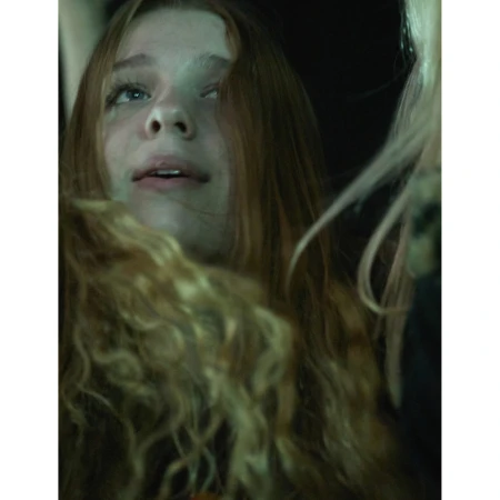 Close-up of a young woman with red hair looking up and to the left, soft light, and dark background.