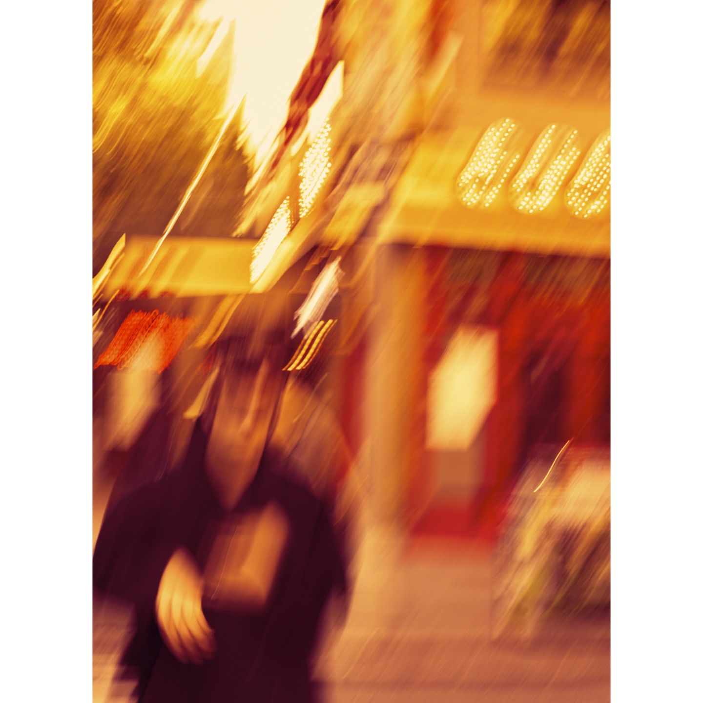 Blurred urban scene with a pedestrian in motion, featuring warm, amber lighting and a storefront facade in the background.