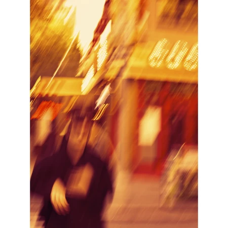 Blurred urban scene with a pedestrian in motion, featuring warm, amber lighting and a storefront facade in the background.