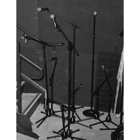 Multiple microphone stands are seen on a stage, arranged on a black surface against a dark background with some stairs visible to the left.